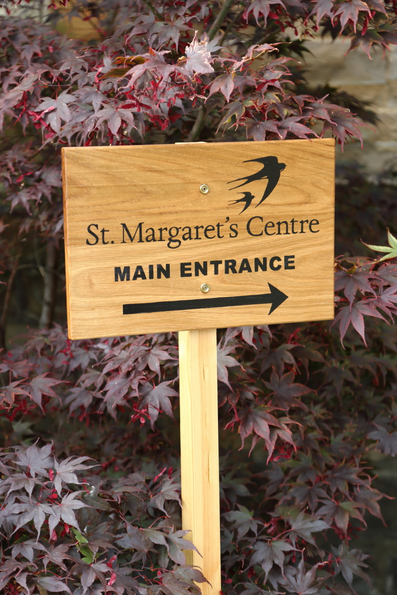 The welcome sign at St Margaret's Centre, with purple leaves in the background